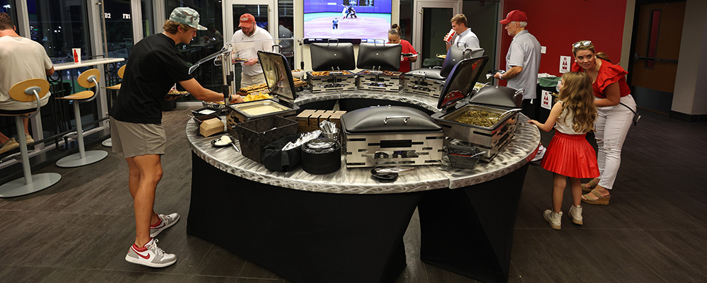 People serving themselves from a large buffet on a circular table