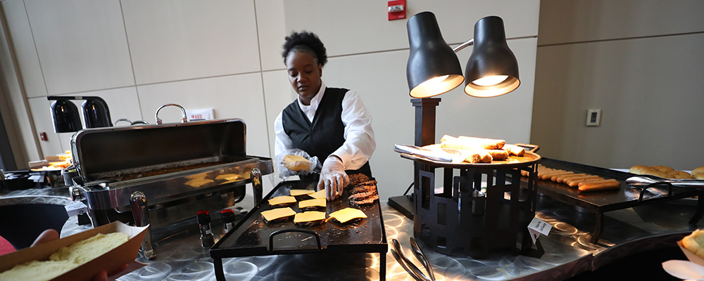 Woman managing a grilling station where she is making hamburgers with sausages and hot dogs nearby